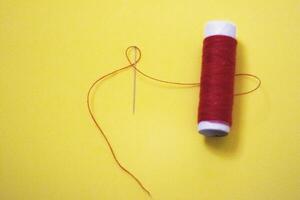 spool of thread with a needle on yelow isolated background photo
