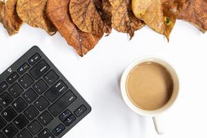 Autumn composition. Home office workspace, woman desk with empty notebook, coffee, keyboard, dry leaves on isolated white background. Autumn, autumn business concept. Flat lay, top view, copy space photo