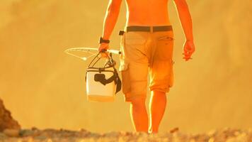 Man, Beach, Sunset. A man walks along a beach carrying a cooler with a sunset behind him. video