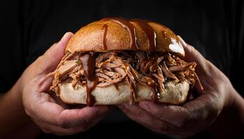 close-up of hands holding a pulled pork sandwich with barbecue sauce dripping down the sides against a dark background photo