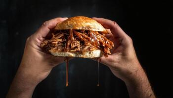 close-up of hands holding a pulled pork sandwich with barbecue sauce dripping from the sides against a dark background photo