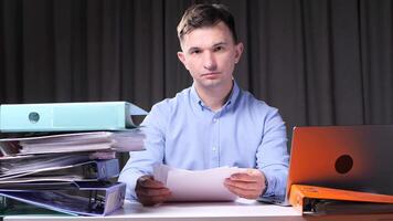 Office worker examining documents at desk with laptop and binders video