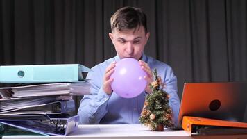 Office worker inflating balloon at christmas time with stack folders and laptop video
