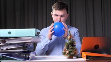 Office worker inflating blue balloon at desk with christmas tree and documents video