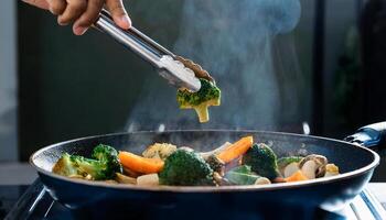 hands lifting steaming broccoli with tongs over vibrant roasted vegetables in a sizzling pan photo