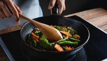 close-up of a chef hands gripping a cast-iron skillet while sauteing colorful vegetables on a rustic wooden surface photo