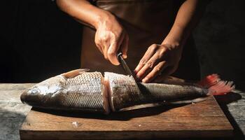 close-up of a chef hands filleting a whole fish with precise cuts on a wooden cutting board, showcasing clean flesh and professional preparation photo