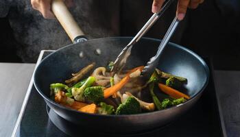 hands turning vibrant vegetables roasting in a steaming pan with tongs over high heat photo