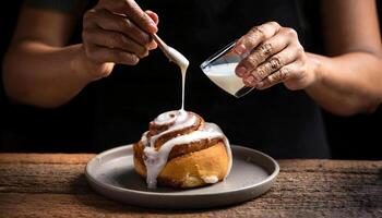 close-up of baker hands glazing a warm cinnamon roll with thick, creamy icing dripping over the edges photo
