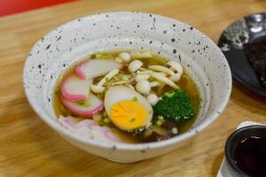 Japanese food concept. Shoyu Ramen with mushroom, pink and white fishballs, boiled egg, and green broccoli in a bowl. photo