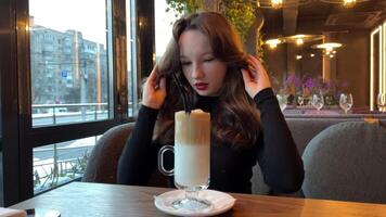 Side view of woman in pajamas drinking coffee in morning and looking out window, slow motion. Greenery on background. Girl relaxing and enjoying video