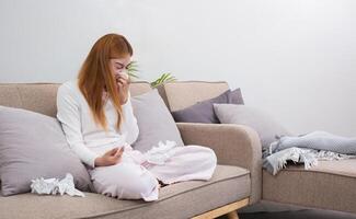 Young Asian woman with cold and allergies feels sick and sneezes on a day of resting at home. photo
