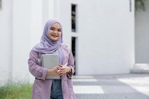 Confident Muslim Girl Student in Hijab Holding Books and Smiling Outdoors, Embracing Education and Modernity in a Bright Urban Setting photo