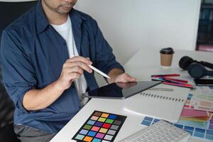 Creative Graphic Designer Planning a New Project with Digital Tablet and Color Swatches in Modern Office Environment photo