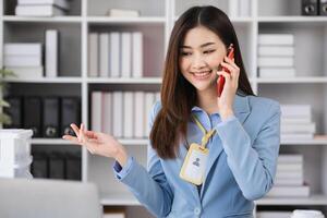 Young Female Accountant in Modern Office Environment, Smiling and Talking on Phone, Professional Businesswoman at Work, Confident and Focused, Office Background with Shelves and Documents photo