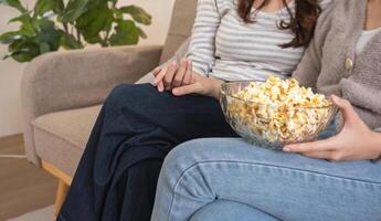 Close-up of two women holding hands with bowl of popcorn on couch. Concept of friendship and comfort photo