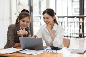 Young Businesswoman Collaborating with Colleague in Modern Office Setting, Discussing Ideas and Analyzing Data on Laptop, Professional Teamwork, and Corporate Collaboration photo