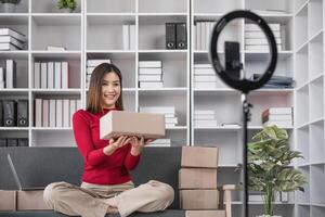Female Business Owner Selling Small Online Products from Home Office, Smiling Woman Holding Package, E-commerce Entrepreneur, Modern Workspace with Shelves and Ring Light photo