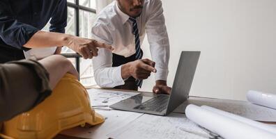 Engineering Team Collaborating on Work Plans Around a Table with Blueprints and Laptop in Modern Office photo