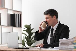 Businessman drinking coffee while working at desk with laptop, concept of break and focus photo