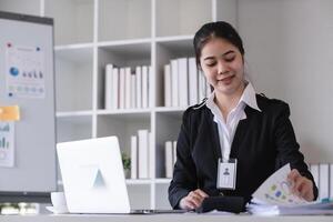 Accountant sitting with financial documents, using laptop, calculating financial and tax figures for company on table in office photo