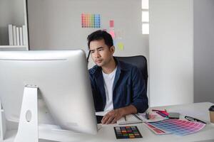 Graphic Designer Focused on Project Planning in Modern Office with Color Swatches and Computer photo