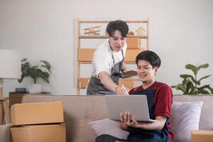 A gay couple running a small business takes order on a laptop and sells product online together in a room full of boxes. photo