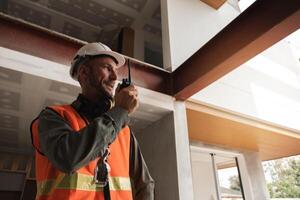 Young Engineer at Construction Site Communicating via Walkie-Talkie, Wearing Safety Gear and Reflective Vest, Overseeing Modern Building Project, Daylight Scene photo