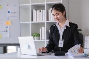 Accountant sitting with financial documents, using laptop, calculating financial and tax figures for company on table in office photo