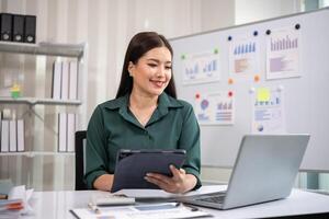 Asian businesswoman working on financial document with laptop on desk in office room photo