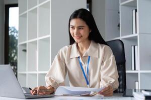Professional Woman Working on Documents at a Modern Office Desk with Laptop and Shelves in Background photo