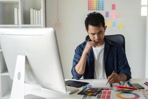 Young Male Graphic Designer Focused on Creative Project at Modern Workspace with Computer and Color Swatches photo