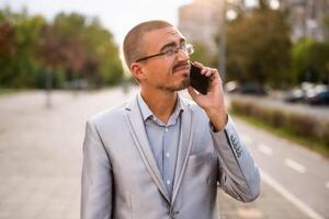 Portrait of distraught businessman who is talking on phone. Young businessman standing in the street and using smartphone. photo