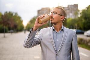 Portrait of young businessman who is standing in the street and drinking coffee to go. photo