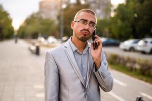 Portrait of distraught businessman who is talking on phone. Young businessman standing in the street and using smartphone. photo