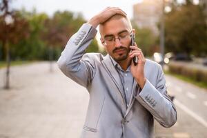 Portrait of distraught businessman who is talking on phone. Young businessman standing in the street and using smartphone. photo