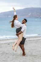 Couple joyfully celebrating on a sandy beach with ocean waves in the background during a cloudy day photo