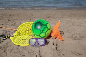 Beach tennis racket and ball of yellow color,swimming mask ,and beach playing ball on tne beach.Copy space.Summer sport background. photo