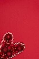 Top view photo heart lined with Christmas lollipops and decorated with Christmas tree toys of red colour,on red background for greeting card. Xmas backdrop with space for text.Copyspace.Vertical photo.