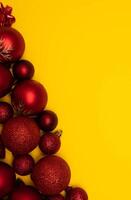 Top view photo tree lined with Christmas tree decorations of red colour on yellow background for greeting card. Xmas backdrop with space for text.Copyspace.Vertical photo.