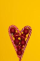 Top view photo heart lined with Christmas lollipops and decorated with Christmas tree toys of red colour,on yellow background for greeting card. Xmas backdrop with space for text.Copyspace.Vertical photo.