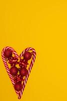 Top view photo heart lined with Christmas lollipops and decorated with Christmas tree toys of red colour,on yellow background for greeting card. Xmas backdrop with space for text.Copyspace.Vertical photo.