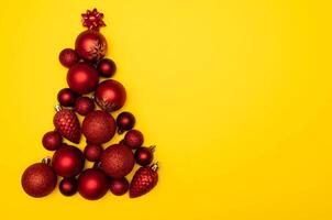 Top view photo tree lined with Christmas tree decorations of red colour on yellow background for greeting card. Xmas backdrop with space for text.Copyspace.