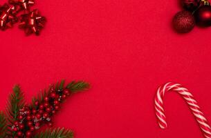 Top view photo christmas tree toys of red colour,spruce branch on red background for greeting card. Xmas backdrop with space for text.Copyspace.