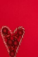 Top view photo heart lined with Christmas lollipops and decorated with Christmas tree toys of red colour,on red background for greeting card. Xmas backdrop with space for text.Copyspace.Vertical photo.