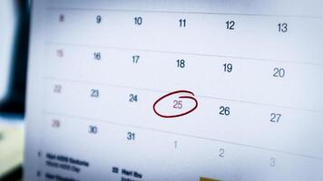 close-up of December 25, 2024, on an office calendar, circled in red marker to indicate a holiday, with a blurred office workspace in the background. photo