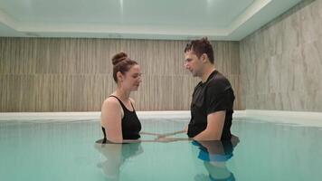 Joyful couple engages in lively conversation while standing in tranquil indoor pool environment. video