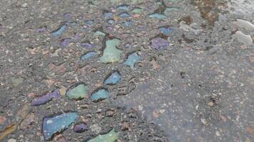 Vibrant oil slick on wet pavement creates colorful patterns with shimmering rainbow reflections in rainy weather. video