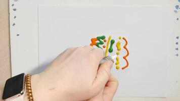 Artistic hand dispensing toothpaste into colorful patterns on white canvas with creative flow and dynamic movement. video