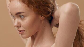 A young woman with flowing curly red hair gazes thoughtfully to the side, her skin glowing softly under warm lighting, creating an intimate and serene atmosphere. video